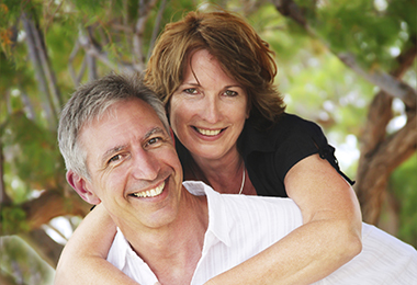 A smiling mature couple embracing outdoors under a tree